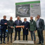 Auf dem Bild ist eine Personengruppe zu sehen. Minister Reul und Landrat Jochen Hagt halten eine Zeitkapsel. Daneben stehen die Landräte aus Olpe und dem Märkischen Kreis, der Geschäftsführer der Firma Sideka sowie ein Vertreter der Investorengemeinschaft. Hinter der Personengruppe ist ein großes Schild der Firma Sideka zu sehen, auf dem der geplante Entwurf des künftigen Trainingszentrums zu sehen ist. Links hinter der Personengruppe steht ein Streifenwagen.